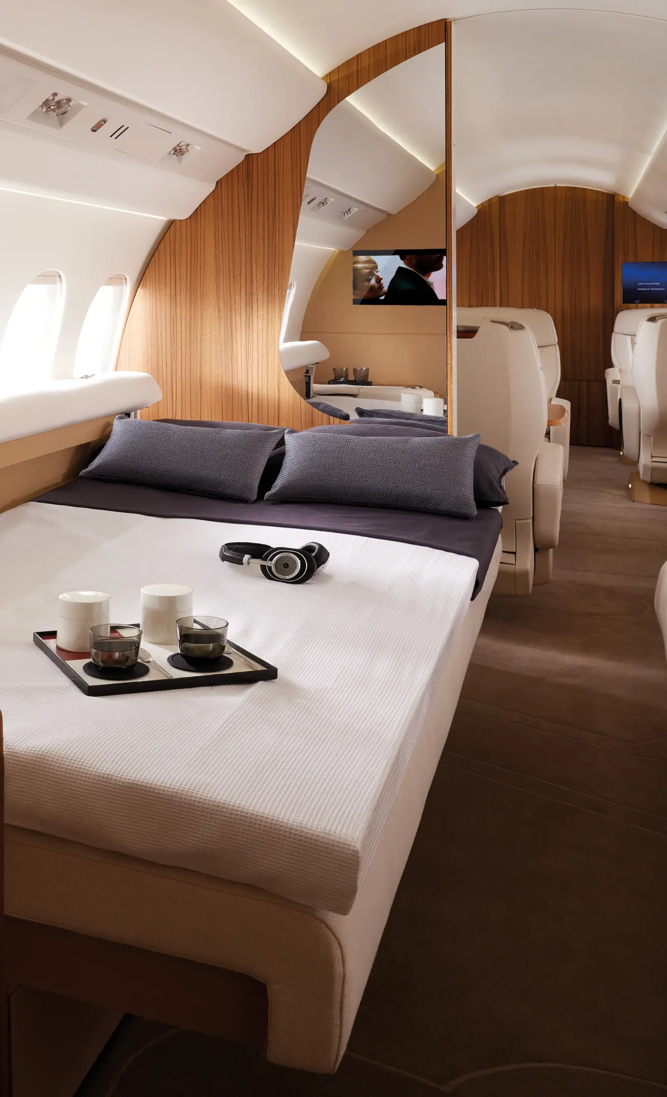 Jet cabin featuring a double-bed with drinks placed on a plateau and a pair of headphones.